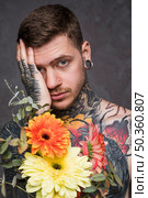 portrait tattooed pierced young man holding flowers hand looking camera. Стоковое фото, агентство Ingram Publishing / Фотобанк Лори
