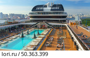 Tokyo, Japan - Oct 2 2024, panoramic view of the public outdoor pool on the upper deck of the MSC Belissima cruise ship, with people relaxing on sun loungers, at daytime, Tokyo, Japan. Редакционное фото, фотограф Сергей Богомяко / Фотобанк Лори