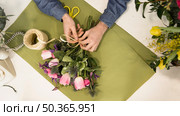 elevated view male tourist tying flower bouquet with string green paper desk. Стоковое фото, агентство Ingram Publishing / Фотобанк Лори