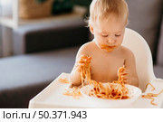 baby boy eating pasta his highchair making mess. Стоковое фото, агентство Ingram Publishing / Фотобанк Лори