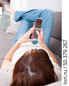 Portrait of a beautiful woman lying on sofa holding a cellphone and sending a sms. Стоковое фото, агентство Ingram Publishing / Фотобанк Лори