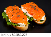 Two delicious smoked salmon canapes with cream cheese, lettuce and capers on fresh toast, healthy appetizer snacks on black background. Стоковое AI-изображение, AI-художник Павел Муравьев / Фотобанк Лори