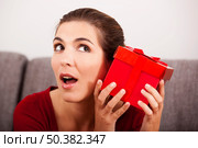 Beautiful and happy woman trying to guess what is inside the christmas present. Стоковое фото, агентство Ingram Publishing / Фотобанк Лори