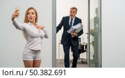 Young female employee taking selfie at work while angry boss enters office, this concept shows inappropriate social media behavior. Стоковое AI-изображение, AI-художник Павел Муравьев / Фотобанк Лори