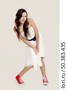 Beautiful young woman wearing a white dress with a pair of red sneakers. Стоковое фото, агентство Ingram Publishing / Фотобанк Лори