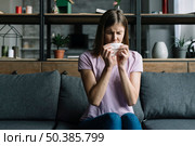 woman sitting sofa blowing nose with tissue paper. Стоковое фото, агентство Ingram Publishing / Фотобанк Лори