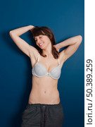 Beautiful young woman wearing a casual lingerie and pajama pants, against a blue wall. Стоковое фото, агентство Ingram Publishing / Фотобанк Лори