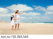 Beautiful pregnant woman and her little daughter on the beach pointing to the sea. Стоковое фото, агентство Ingram Publishing / Фотобанк Лори