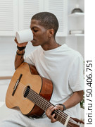 male musician home playing guitar drinking from mug. Стоковое фото, агентство Ingram Publishing / Фотобанк Лори