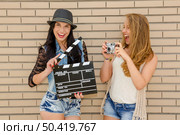 Two beautiful and young girlfriends holding a clapboard, in front of a brick wall. Стоковое фото, агентство Ingram Publishing / Фотобанк Лори