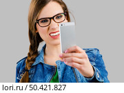 Beautiful woman taking a selfie and making a ugly face, isolated over a grey background. Стоковое фото, агентство Ingram Publishing / Фотобанк Лори