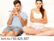 Addicted young man on bed with a cellphone while the woman looks angry. Стоковое фото, агентство Ingram Publishing / Фотобанк Лори