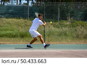 Tennis player hitting backhand at ball with racket on court. Стоковое фото, агентство Ingram Publishing / Фотобанк Лори