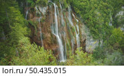 Wide waterfall flows down steep cliffs by greenery at Plitvice Lakes in Croatia. Стоковое видео, видеограф Igor Tichonow / Фотобанк Лори