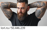 Brutal attractive bearded biker man with tattooed hands poses in black blank t-shirt from premium thin cotton, isolated on white mockup. Стоковое AI-видео, аниматор Sergey Grishin / Фотобанк Лори