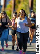 Several overweight women in athletic clothing are sprinting down a busy city street, displaying determination and focus. Стоковое AI-изображение, AI-художник Данила Большаков / Фотобанк Лори