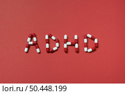 ADHD abbreviation formed of pharmaceutical pills on red background. Attention deficit hyperactivity disorder and mental health awareness.. ADHD formed of pharmaceutical pills. Стоковое фото, агентство Ingram Publishing / Фотобанк Лори