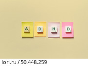 ADHD abbreviation formed of scrabble tiles on sticky notes over beige background. Attention deficit hyperactivity disorder and mental health awareness.. ADHD formed of scrabble tiles on sticky notes. Стоковое фото, агентство Ingram Publishing / Фотобанк Лори