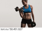Beautiful young woman in a workout gear lifting dumbbells. Стоковое фото, агентство Ingram Publishing / Фотобанк Лори
