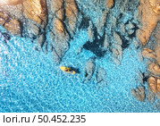 Aerial view of man on floating sup board on blue sea, rocky beach at sunset in summer in Sardinia, Italy. Tropical landscape. Kayak on crystal clear water and stones. Top view from drone of canoe. Стоковое фото, агентство Ingram Publishing / Фотобанк Лори
