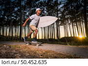 Surf skater rolling by the pine forest at sunset with his surfboard in Maceda, Ovar - Portugal. Стоковое фото, агентство Ingram Publishing / Фотобанк Лори