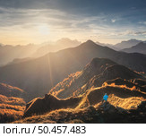 Aerial view of man on the hill and beautiful mountains in haze at colorful sunset in autumn. Dolomites, Italy. Top view of guy, mountain ridges in fog, orange grass and trees, sky in fall. Hiking. Aerial view of man on the hill and beautiful mountains in haze. Стоковое фото, агентство Ingram Publishing / Фотобанк Лори