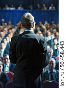 A man stands confidently in front of a large crowd of diverse people, giving a speech or presentation. Стоковое AI-изображение, AI-художник Данила Большаков / Фотобанк Лори