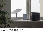 KYIV, UKRAINE - JANUARY 24, 2023: Starlink antenna behind window, wi-fi router and Ecoflow generator on windowsill in cozy apartment interior.. KYIV, UKRAINE - JANUARY 24, 2023: Starlink antenna behind window, wi-fi router and Ecoflow generator on windowsill in cozy home interior. Редакционное фото, агентство Ingram Publishing / Фотобанк Лори