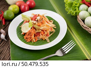 Thai papaya salad in a white plate on banana leaves with lime, tomatoes, eggplant, chili, garlic, peppers, salad, and peanuts. Стоковое фото, агентство Ingram Publishing / Фотобанк Лори