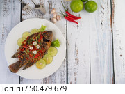 Fried tilapia with chili sauce, lemon salad and garlic on a plate on a white wooden table. Стоковое фото, агентство Ingram Publishing / Фотобанк Лори