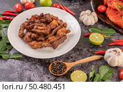 Pork cutlet in a white plate with pepper seeds, kaffir lime leaves, lemons, chilies, garlic on black cement. Стоковое фото, агентство Ingram Publishing / Фотобанк Лори