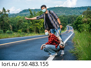 Female tourists sit, male tourists, pretend to hitchhiker Both wearing a mask and on the side of the road. Стоковое фото, агентство Ingram Publishing / Фотобанк Лори