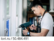 The carpenter holds the drill and drills the window. Selective focus. Стоковое фото, агентство Ingram Publishing / Фотобанк Лори