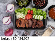 Fried pork topped with sesame, complete with tomatoes, cucumbers, cabbage, and lettuce placed in a black dish. Стоковое фото, агентство Ingram Publishing / Фотобанк Лори