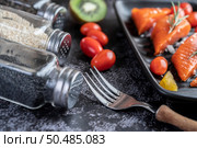 Raw salmon fillets, pepper, kiwi, pineapples, and rosemary onto a plate and black cement floor.Selective focus fork. Стоковое фото, агентство Ingram Publishing / Фотобанк Лори