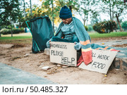 a man sitting beggars with homeless please help message. Selective focus. Стоковое фото, агентство Ingram Publishing / Фотобанк Лори
