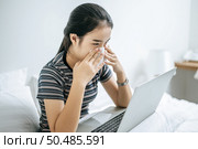 Woman playing laptop and hold a tissue to wipe a nose. Стоковое фото, агентство Ingram Publishing / Фотобанк Лори