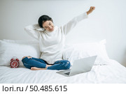 That woman sat on the bed, raised her hand, and put the laptop on the pillow. Стоковое фото, агентство Ingram Publishing / Фотобанк Лори