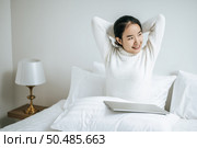 That woman sat on the bed, raised her hand, and put the laptop on the pillow. Стоковое фото, агентство Ingram Publishing / Фотобанк Лори