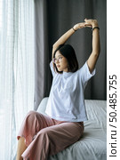 A woman in a white shirt sitting on the bed and raising both arms. Стоковое фото, агентство Ingram Publishing / Фотобанк Лори