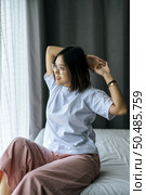 A woman in a white shirt sitting on the bed and raising both arms. Стоковое фото, агентство Ingram Publishing / Фотобанк Лори