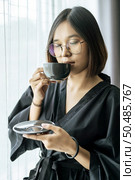 The woman wore a black robe near the window and drank coffee in the bedroom. Стоковое фото, агентство Ingram Publishing / Фотобанк Лори