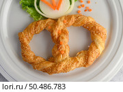 Top view Freshly baked soft pretzel with generous sprinkling of coarse salt and sesame on white dish, decorate with lettuce and carrot beautifully, copy space. Стоковое фото, агентство Ingram Publishing / Фотобанк Лори