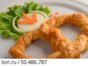 Freshly baked soft pretzel with generous sprinkling of coarse salt and sesame on white dish, decorate with lettuce and carrot beautifully, copy space. Стоковое фото, агентство Ingram Publishing / Фотобанк Лори