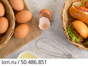 Top view with yolk in glass bowl and in wicker basket, hamburgers and hotdog with slice tomato and lettuce in weave basket, oil in cup and egg whisk placed nearly. Стоковое фото, агентство Ingram Publishing / Фотобанк Лори
