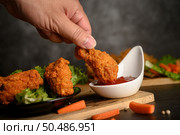 Hand holding crispy fried chicken dipped in tomato sauce. Selective focus. Стоковое фото, агентство Ingram Publishing / Фотобанк Лори