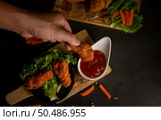 Hand holding crispy fried chicken dipped in tomato sauce. Selective focus. Стоковое фото, агентство Ingram Publishing / Фотобанк Лори