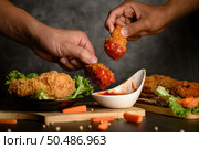 Two hand holding crispy fried chicken dipped in tomato sauce.Selective focus. Стоковое фото, агентство Ingram Publishing / Фотобанк Лори