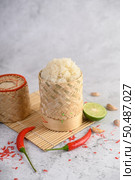 Thai sticky rice in a woven bamboo basket on a wooden panel with chilies, lime, and garlic. Selective focus. Стоковое фото, агентство Ingram Publishing / Фотобанк Лори