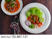 Top View Spicy salad of sardine with tomato sauce mixed with herb and arranged nicely in white dish and sparken stainless spoon and fork over napkin on wooden table, copy space. Стоковое фото, агентство Ingram Publishing / Фотобанк Лори